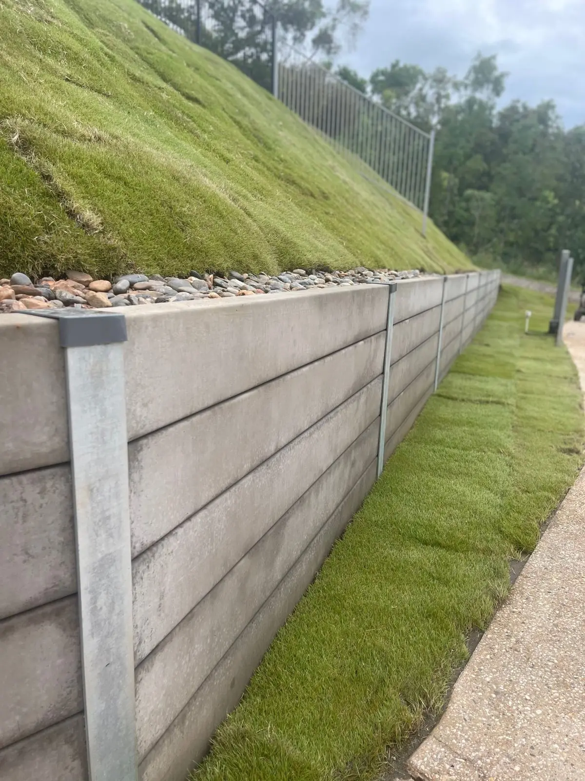 Concrete sleeper retaining wall with river rock and new turf