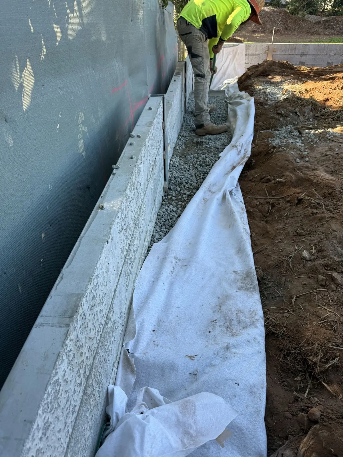 Geofabric and drainage gravel behind a concrete sleeper retaining wall