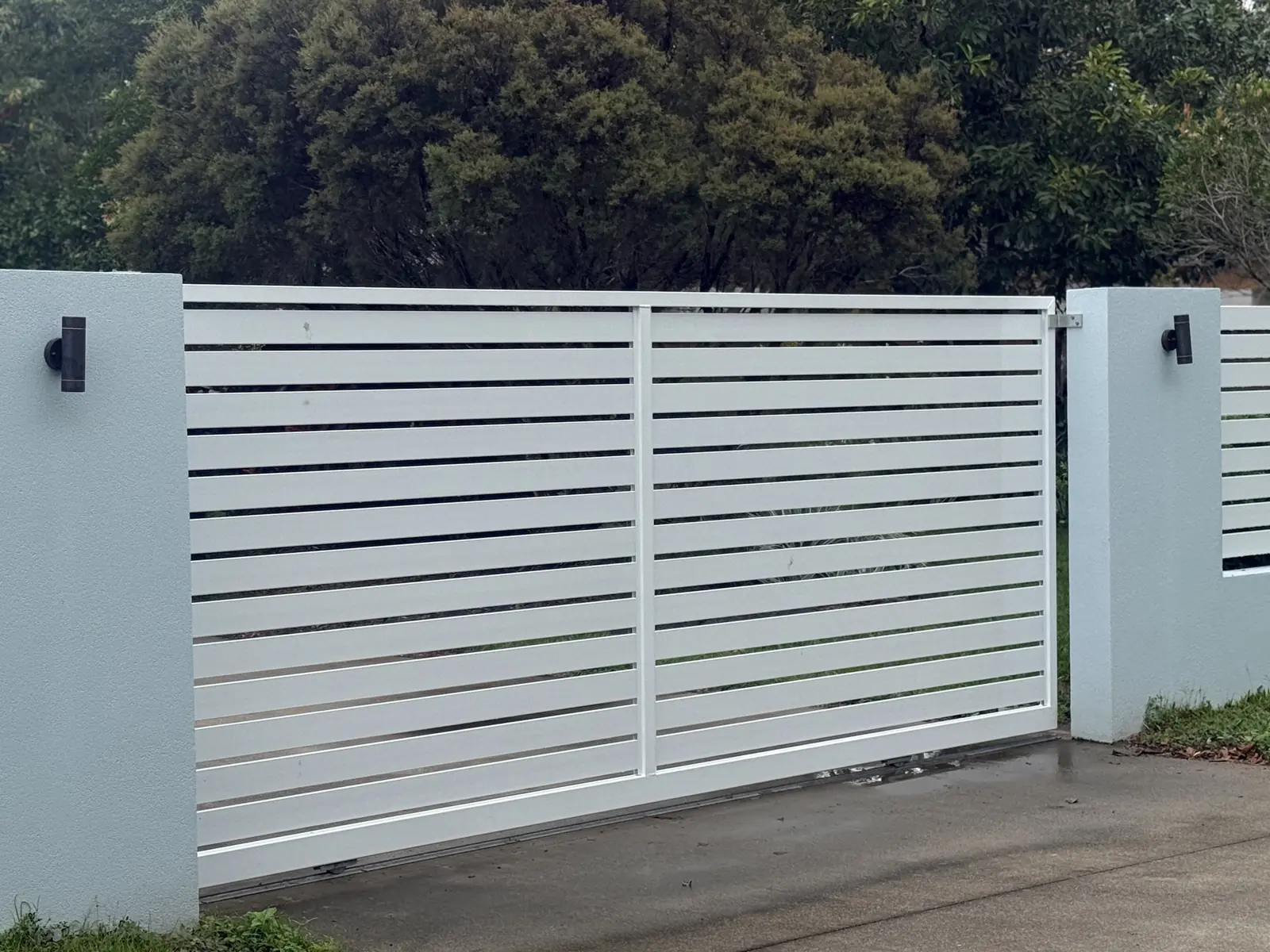 White aluminium slat sliding gate between rendered piers